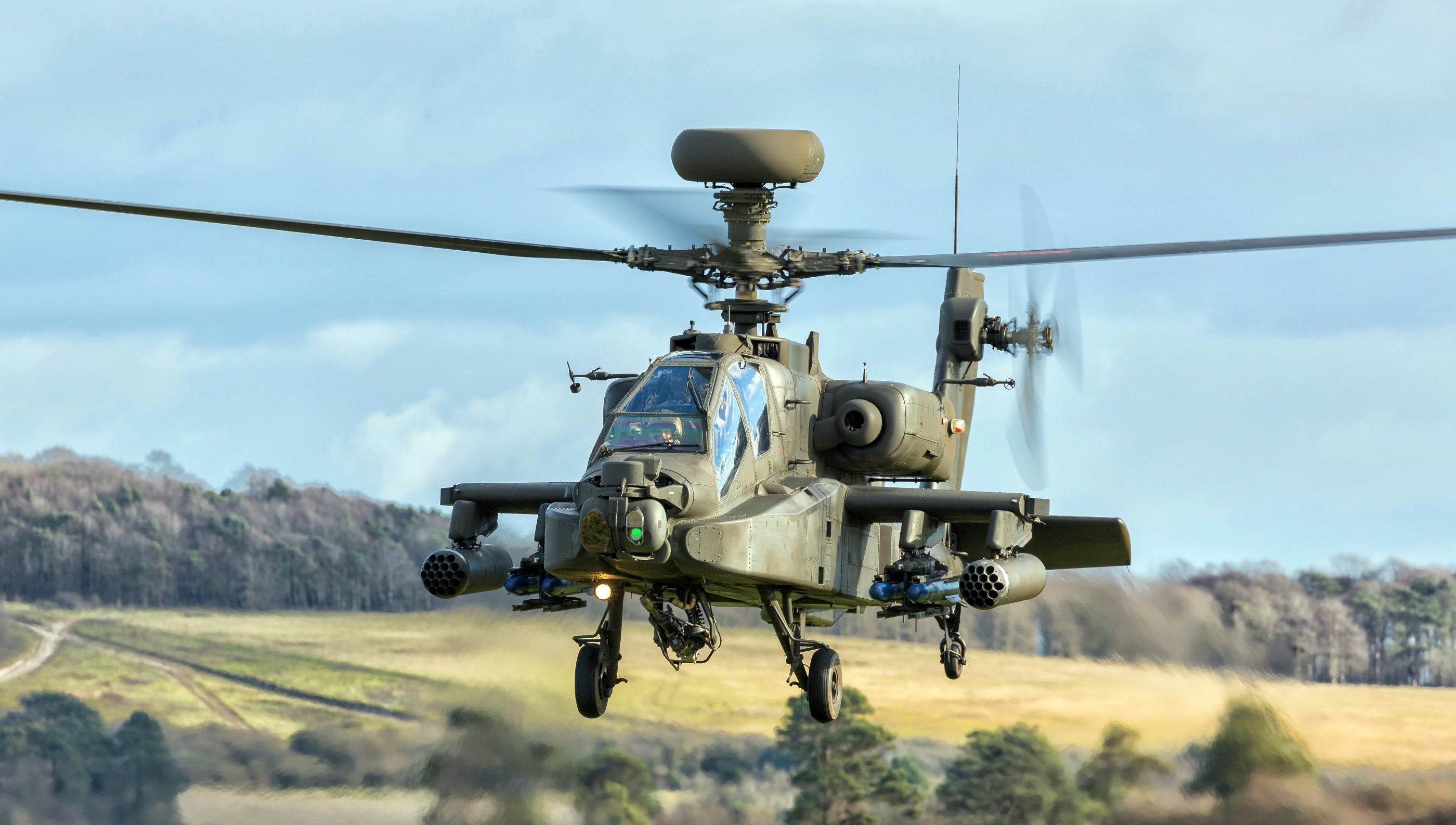 Military attack helicopter flying low over a rural landscape